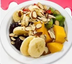 Plato de ensalada de frutas con banano, mango, kiwi y almendras.